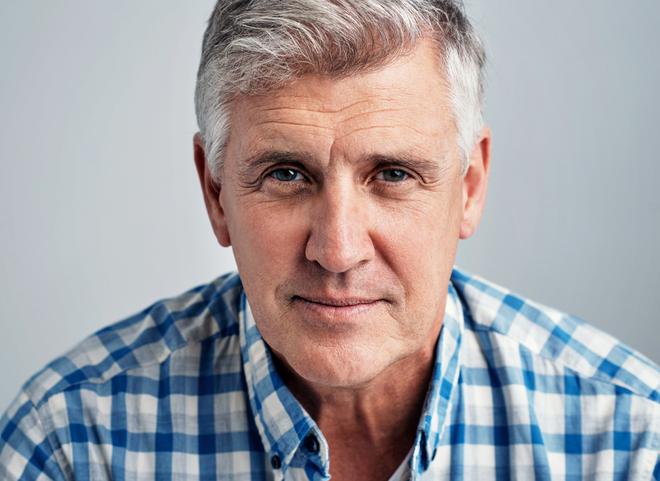 Studio portrait of a mature man posing against a gray background
