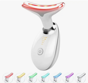 A sleek white and silver face massager with a red LED light at the top. It features a power button and small icon indicators. Below are six color variations.