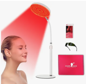 A woman enjoys red light therapy from a floor lamp emitting a glowing red beam. Nearby are sunglasses, a booklet, and a red Akari Shin box.