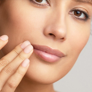 Close-up of a woman with clear skin gently touching her full, pink lips with her fingertips.