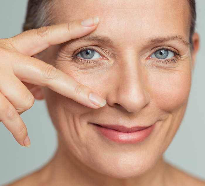 Portrait of smiling senior woman with perfect skin showing victory sign near eye