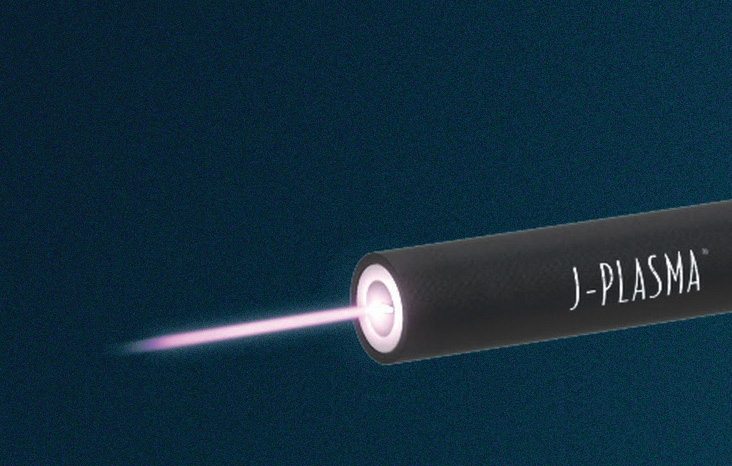 A dark J-Plasma device emitting a narrow beam of purplish-white plasma against a deep navy blue background.